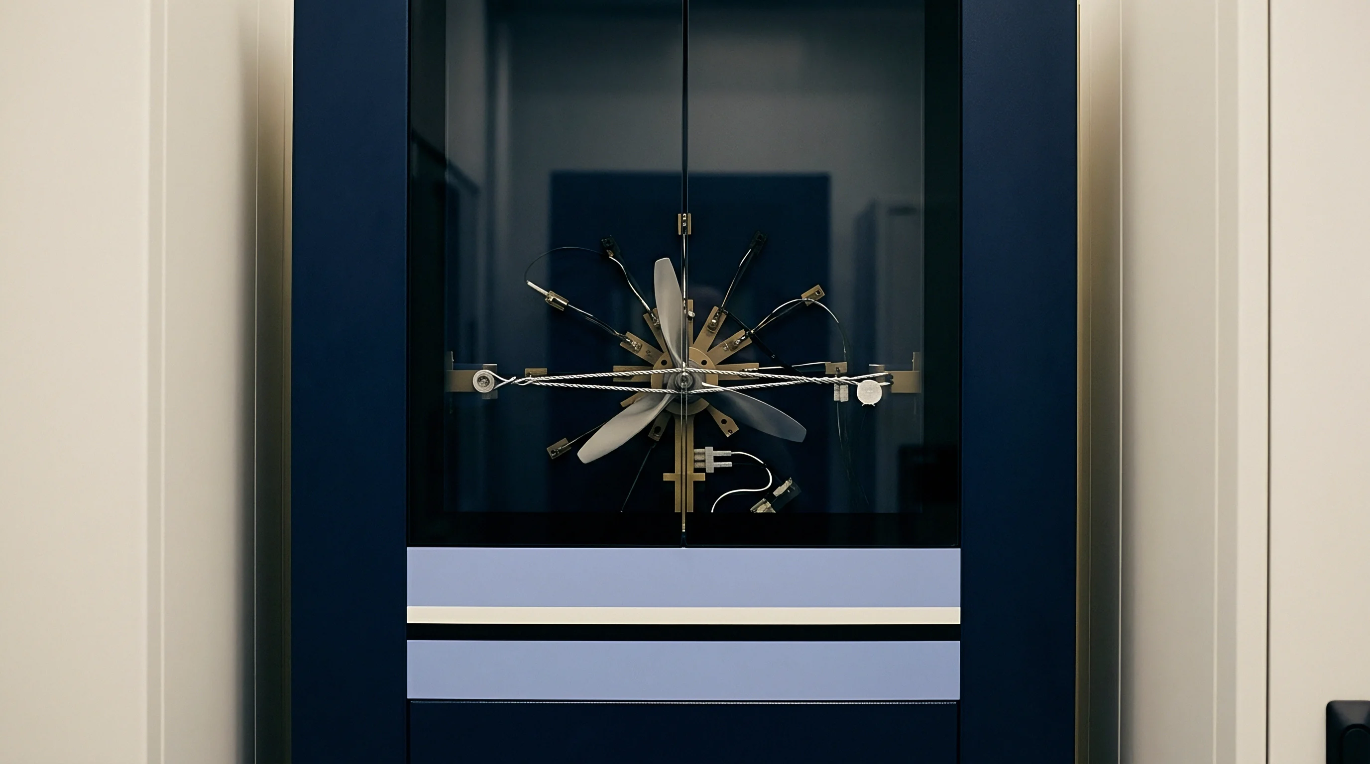 A brass multi bladed measurement rotor with tension cords sits inside a deep blue testing cabinet within a metrology facility.