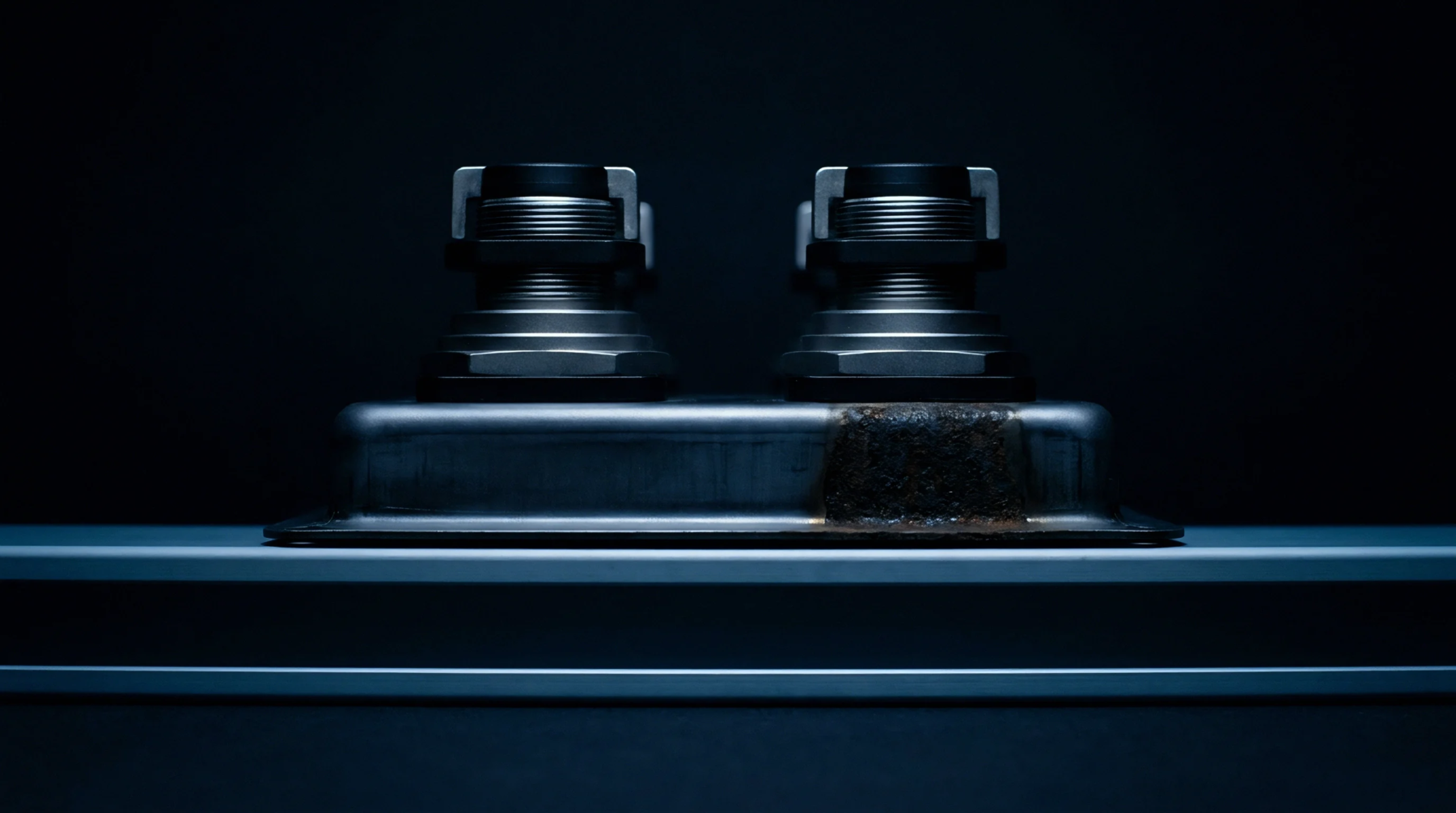 Two identical industrial connectors sit upon a rectangular metal flange resting on a horizontal platform within a low illumination inspection environment.